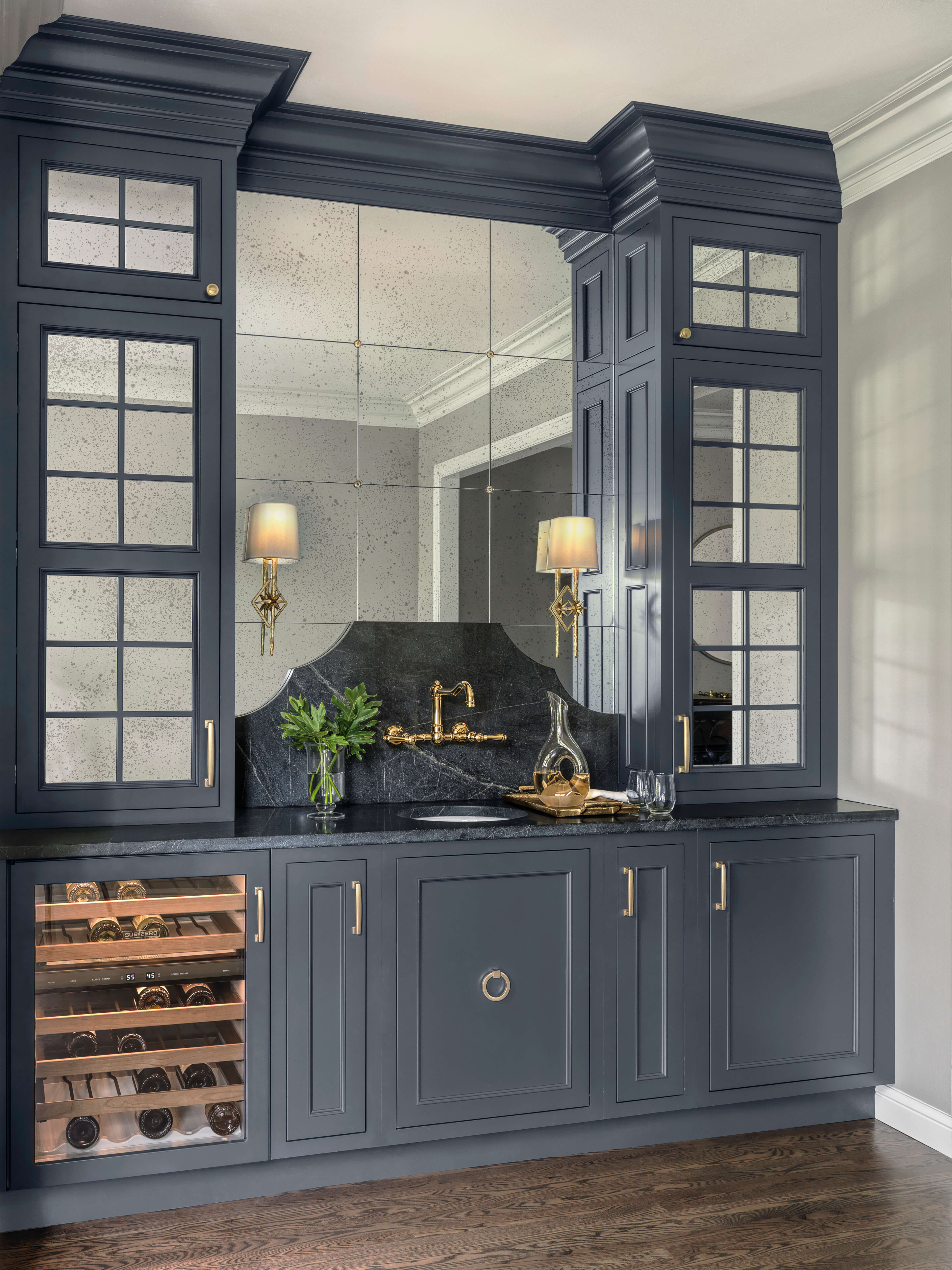 A dark, navy blue pained wet bar design featuring traditional styled inset cabinets and mirrored mullion cabinet doors