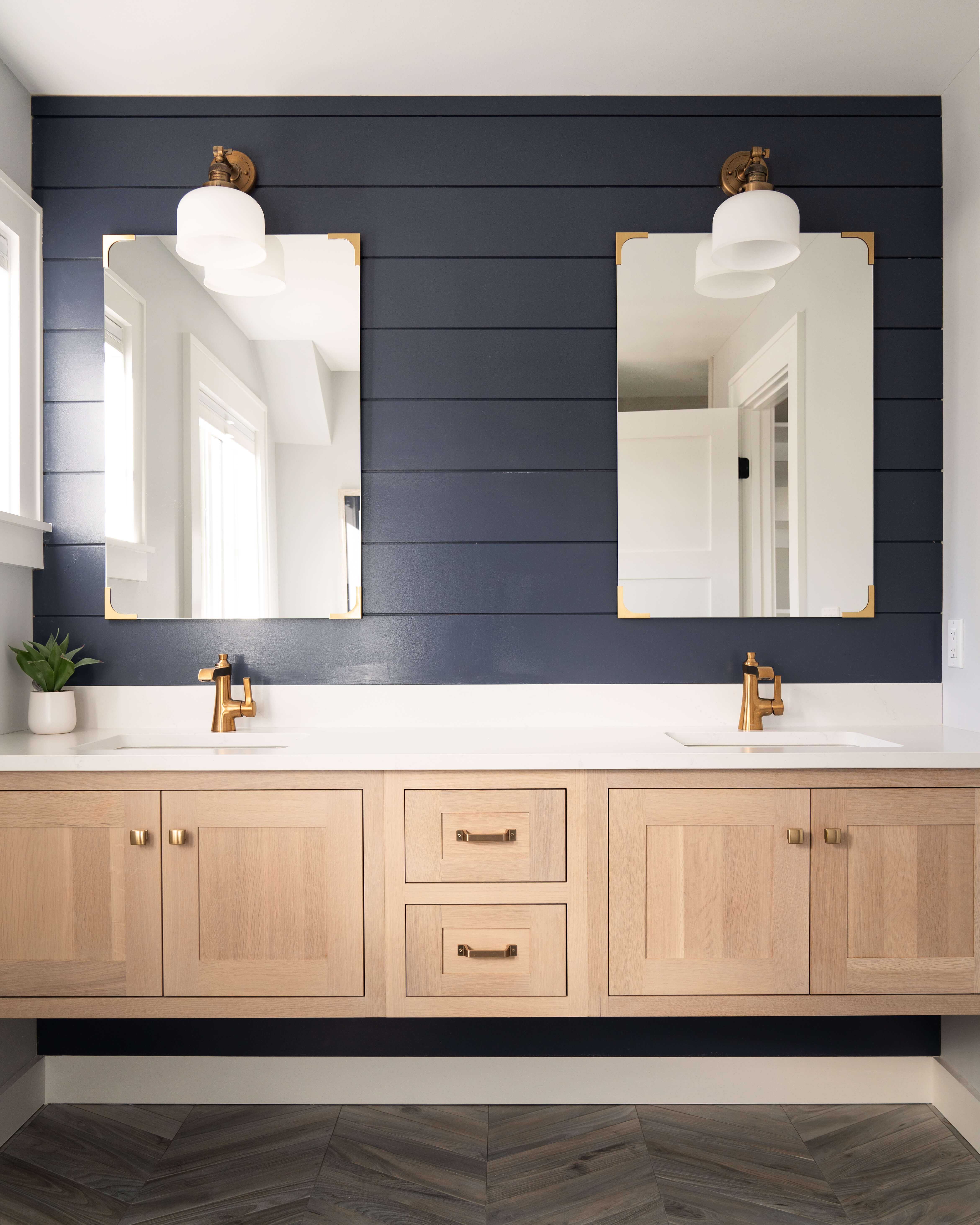 A modern farmhouse bathroom with a transitional styled floating vanity featuring inset style cabinets in a light stained rift sawn white oak. The accent wall behind features navy blue pained shiplap.