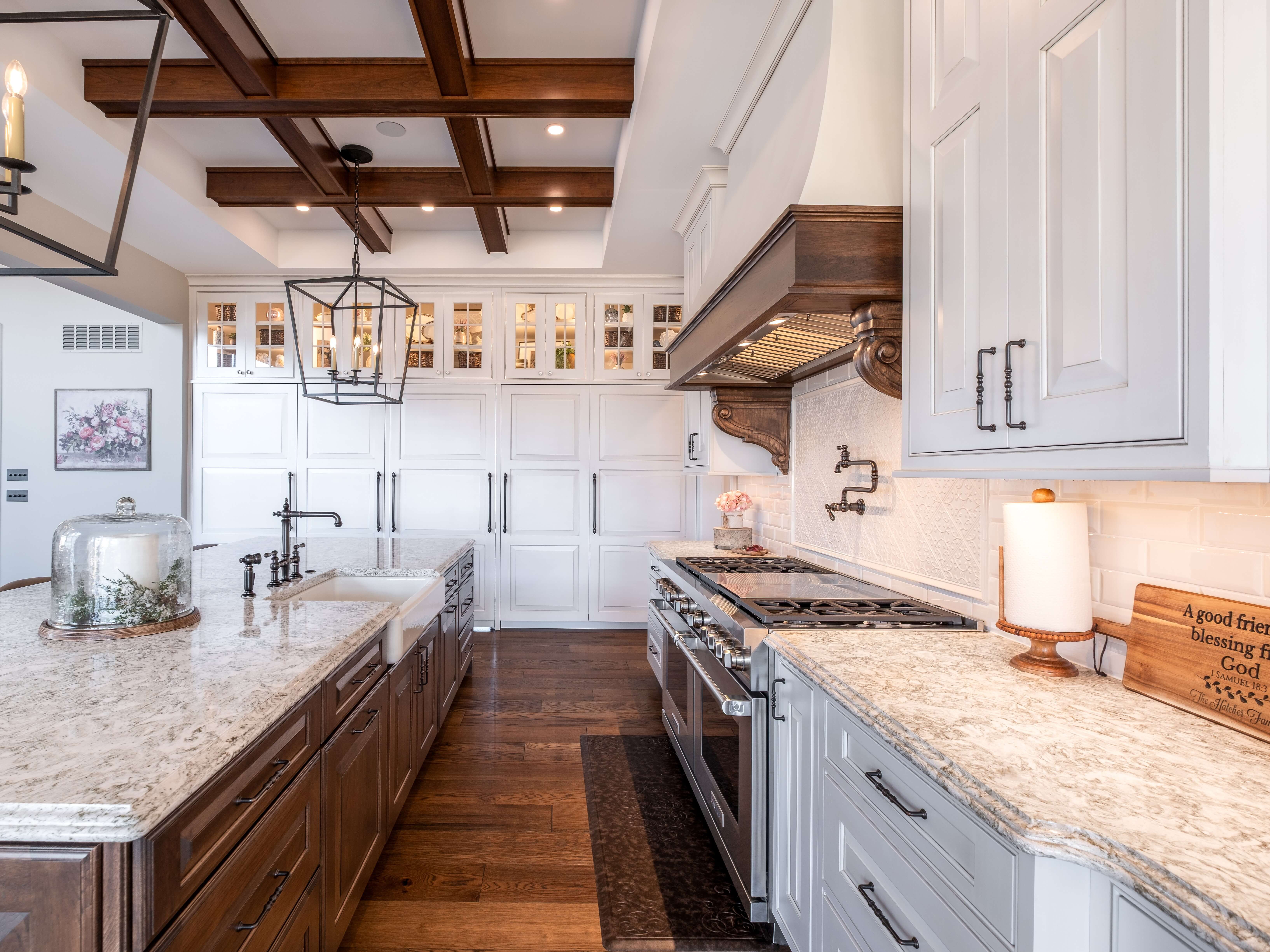 This traditional style kitchen design features inset cabinet doors with raised panel styling as well as a vaulted ceiling with large beams, a kitchen island, and a decorative two-tone wood hood.