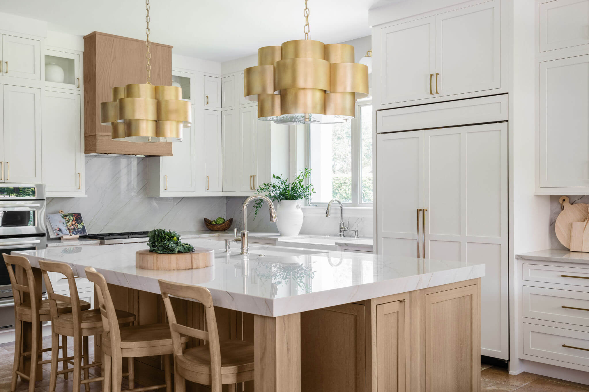 An on-trend kitchen design with transitional styled inset cabinets shown in a white paint and light stained quarter-sawn white oak with glimmers of gold accents.