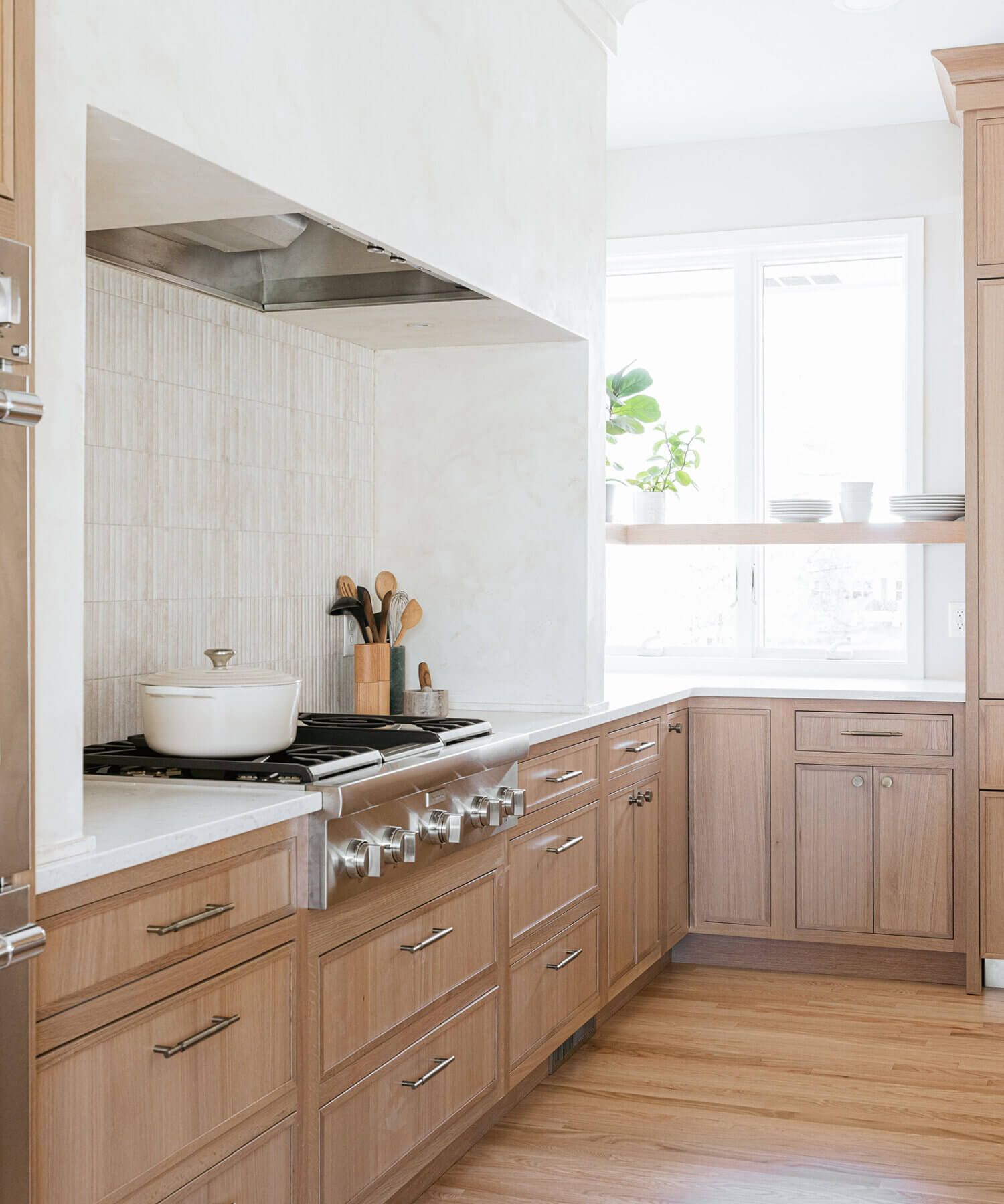 A modern farmhouse kitchen featuring light stained quarter-sawn white oak wood cabinets with a sleek micro, skinny shaker doors style and bright white countertops. A white range alcove frames the cooking area.