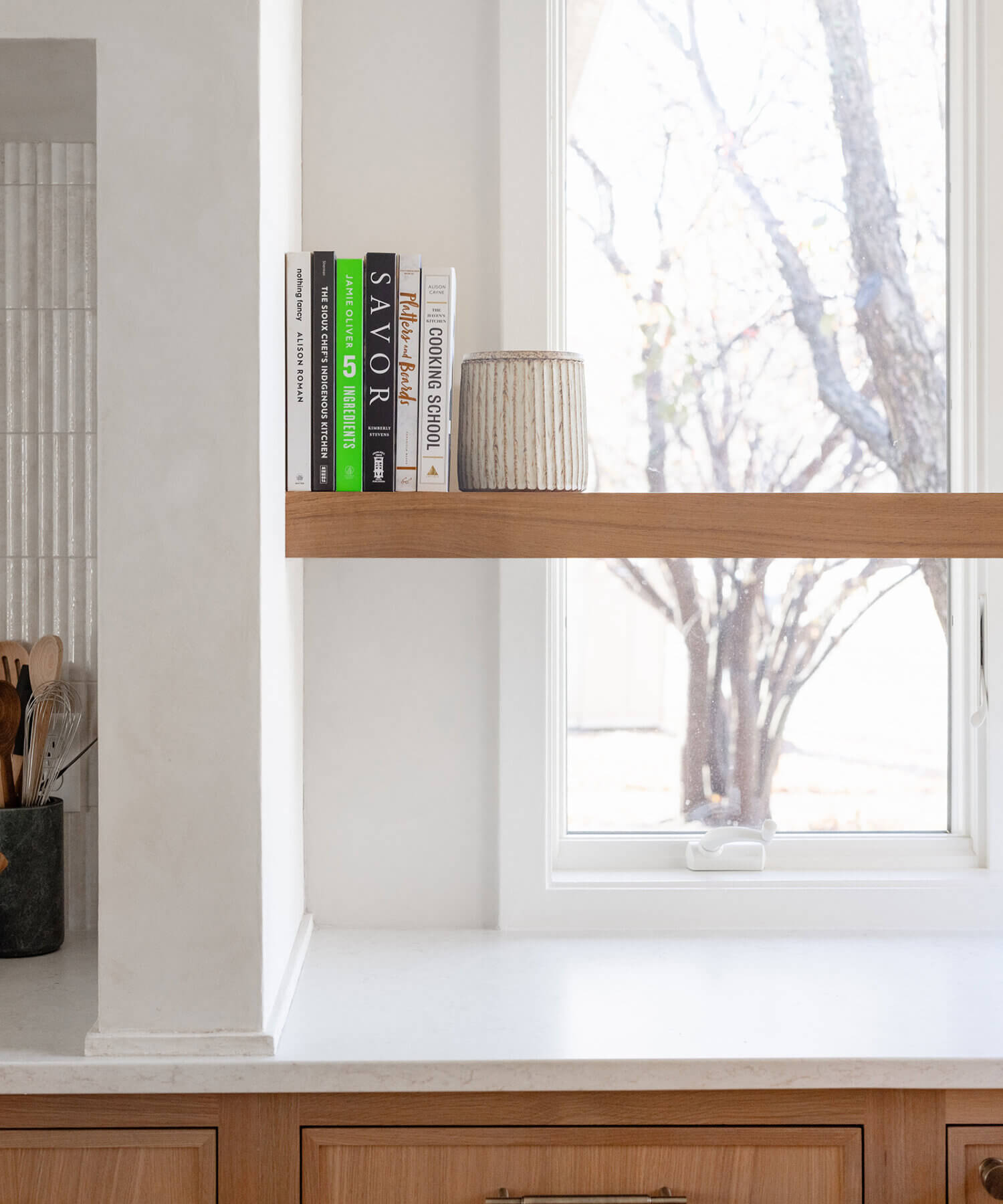 The corner windows of the kitchen feature a corner floating shelf made with Quarter-Sawn White Oak for displaying decor and caring for small house plants.