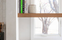 The corner windows of the kitchen feature a corner floating shelf made with Quarter-Sawn White Oak for displaying decor and caring for small house plants.