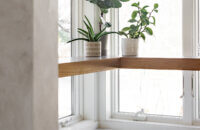 The corner windows of the kitchen feature a corner floating shelf made with Quarter-Sawn White Oak for displaying decor and caring for small house plants.