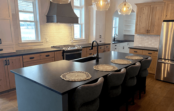An L-shaped kitchen with Knotty Alder cabinets and a green kitchen island and modern wood hood.